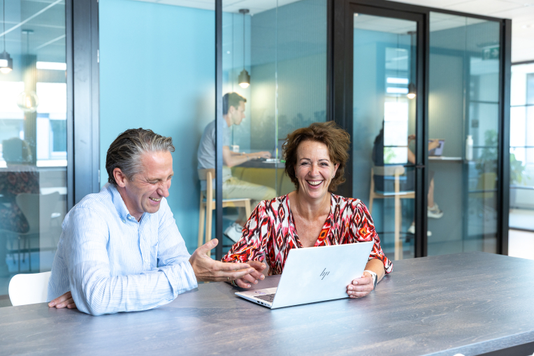 Twee collega's van ActiZ zitten bij een laptop en lachen