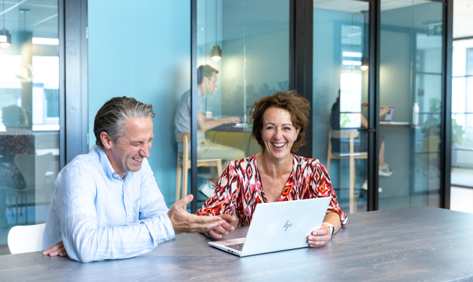 Twee collega's van ActiZ zitten bij een laptop en lachen