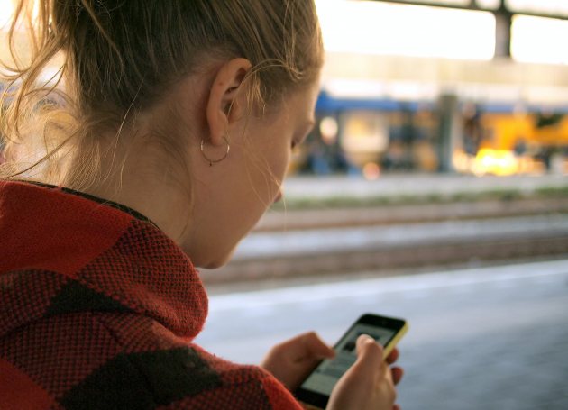 Meisje op perron met telefoon in handen